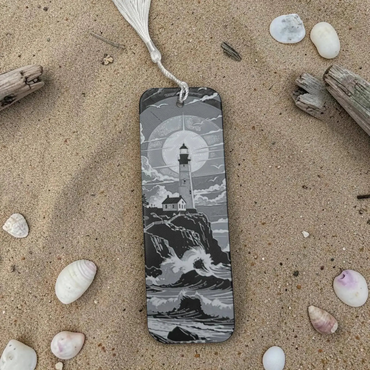 Marque-page phare océan en noir et blanc posé sur sable