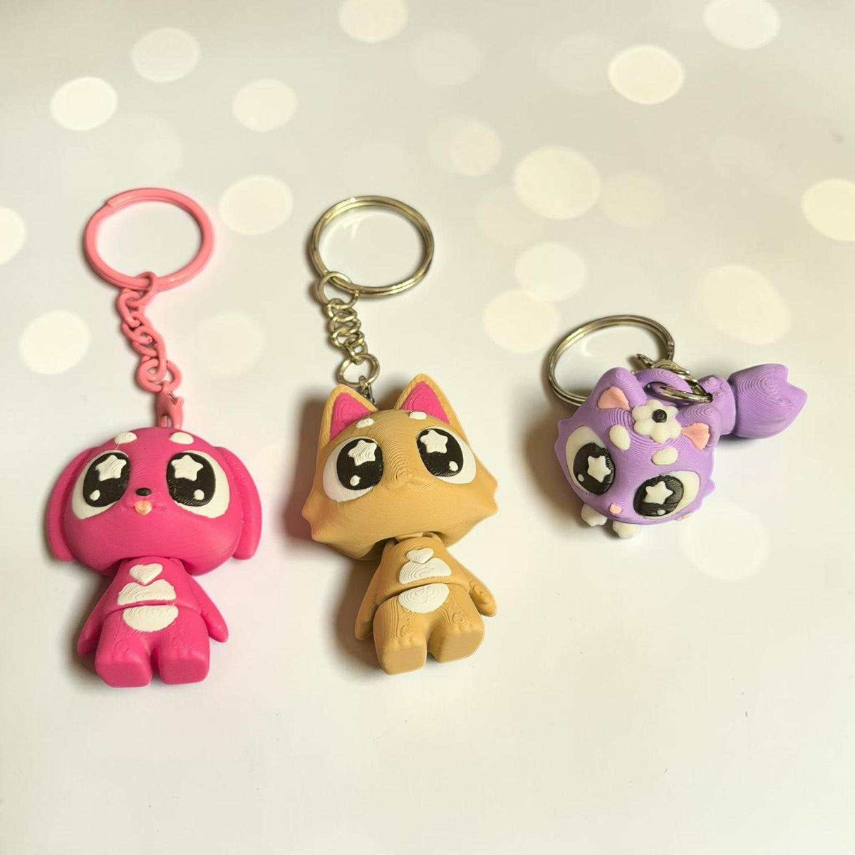 Trois porte-clés en peluche colorés avec figurines d’animaux kawaii rose, beige et violet aux yeux étoilés moins de 10€