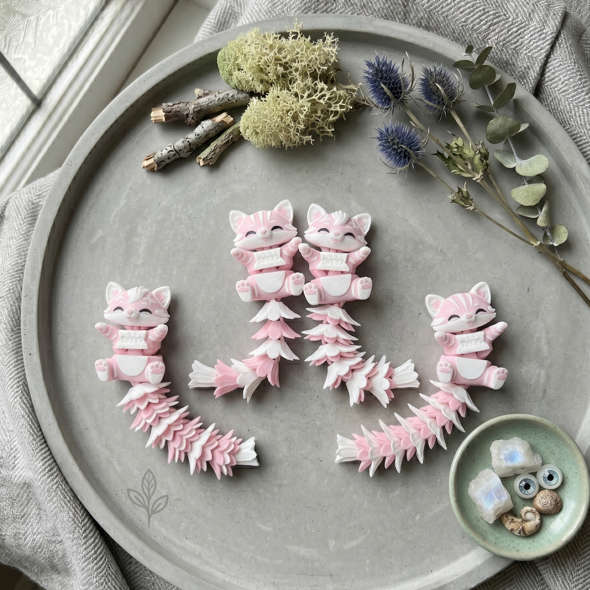 Quatre porte-clés chats articulés roses et blancs présentés dans un décor naturel