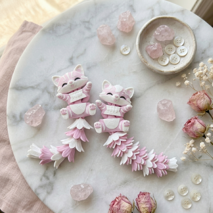 Deux chats articulés kawaii avec longues queues duveteuses sur un décor marbré