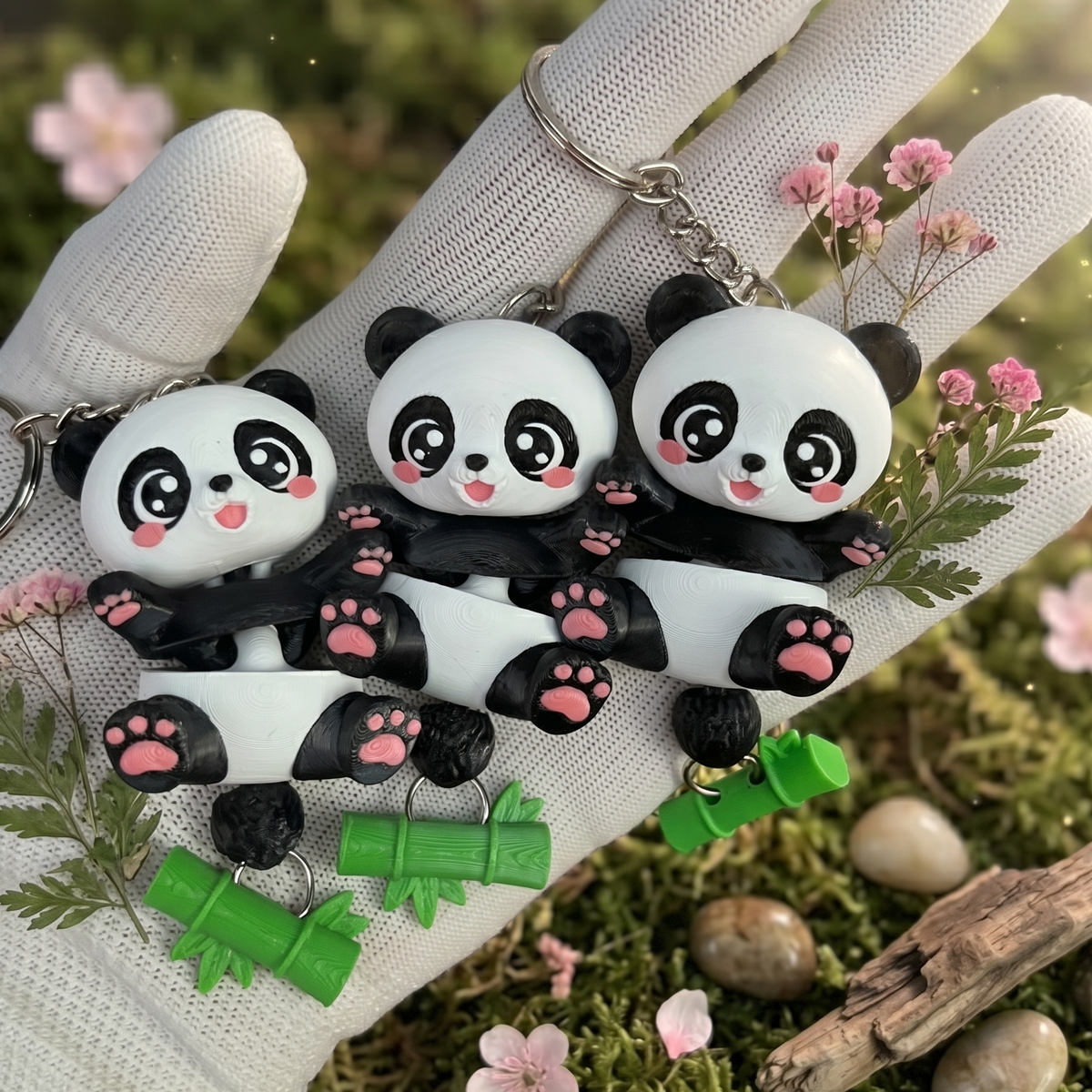 Trois porte-clés pandas articulés kawaii présentés dans un décor fleuri