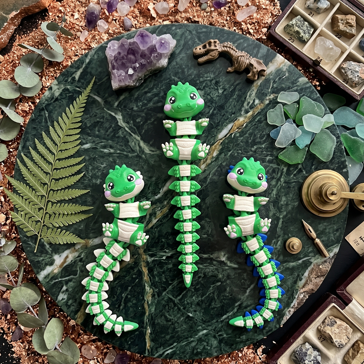 Trois crocodiles articulés kawaii présentés dans un décor de minéraux et de fougères