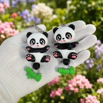 Deux porte-clés pandas articulés kawaii avec chaînettes métalliques dans un jardin fleuri