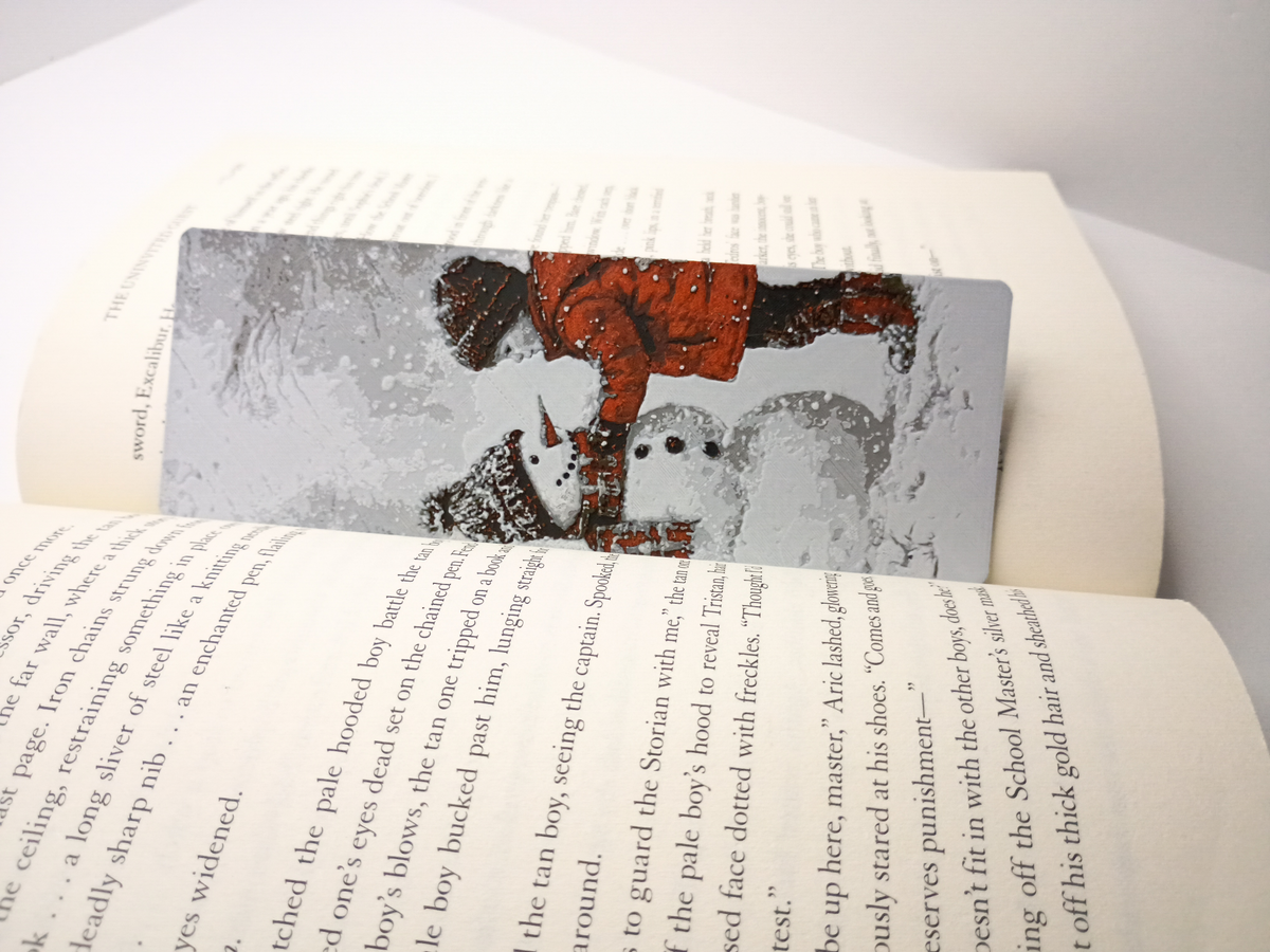 Marque-page de Noël modèle garçon construisant un bonhomme de neige placé dans un livre