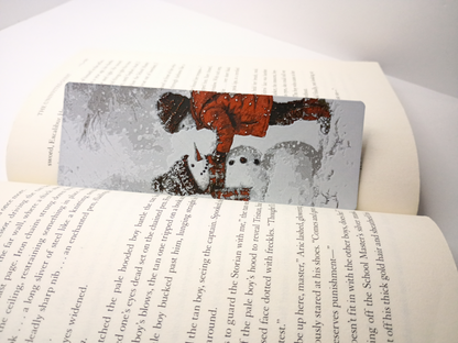 Marque-page de Noël modèle garçon construisant un bonhomme de neige placé dans un livre