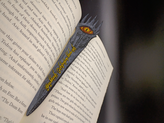 Marque-page 3D Œil de Sauron noir et doré posé dans un livre