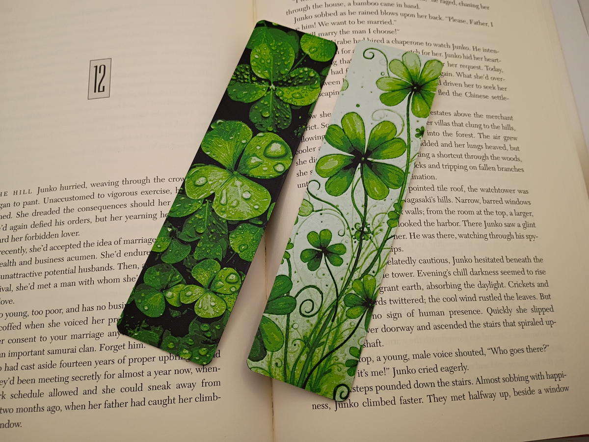 Détail des deux marque-pages Lucky Clovers sur un livre, motifs de trèfles verts porte-bonheur