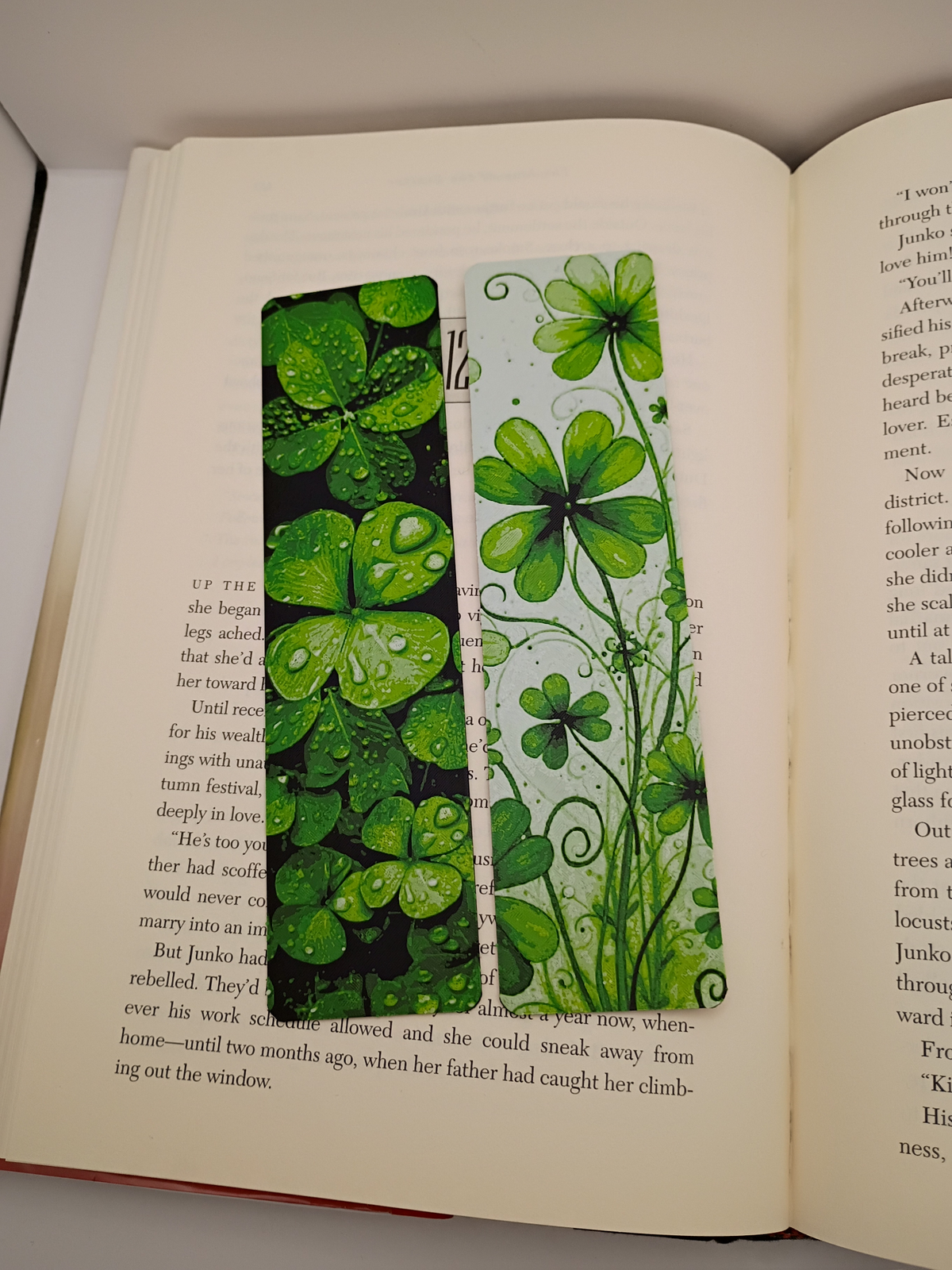 Les deux marque-pages Lucky Clovers posés sur une page de livre, trèfles verts sur fond noir et fond clair
