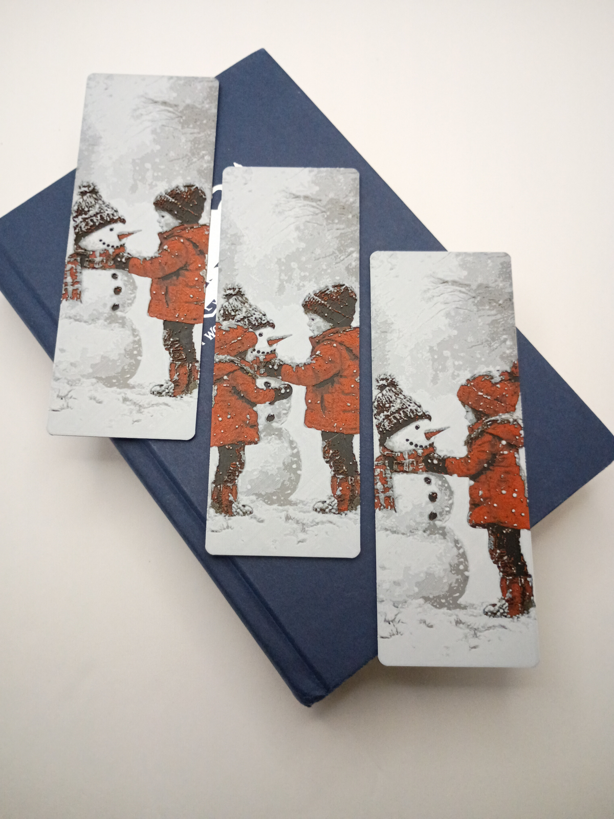Trois marque-pages de Noël avec enfants construisant un bonhomme de neige sur un livre