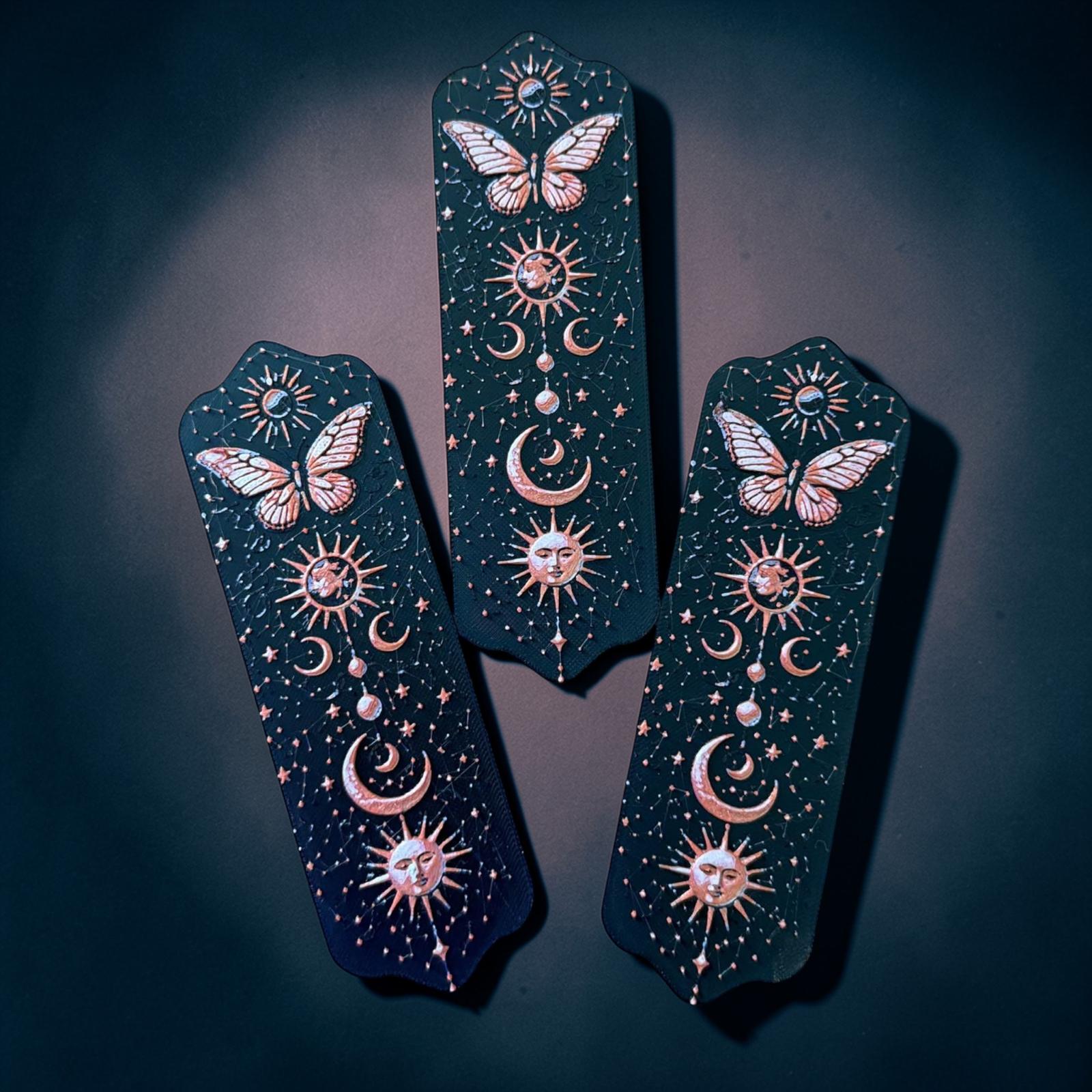 Marque-page papillon céleste en impression 3D avec motifs lune, soleil et étoiles sur fond noir
