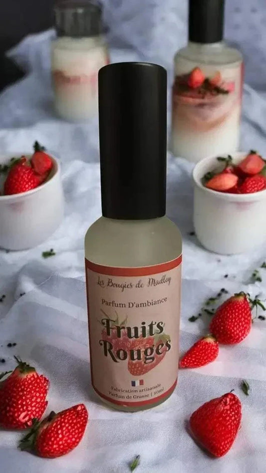 Parfums d’ambiance spray Fruits Rouges avec flacon en verre et bouchon noir, entouré de fraises rouges fraîches.