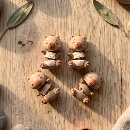 Quatre modèles de porte-clés capybaras avec ventre marron ou crème sur fond bois