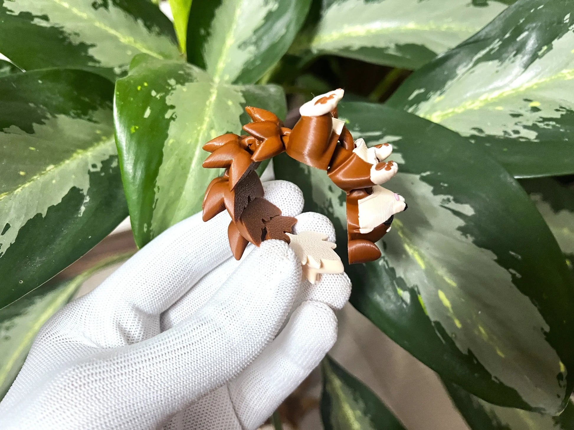 Petit chien articulé Flexi tenu dans une main devant des plantes vertes
