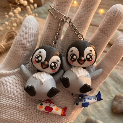 Deux porte-clés pingouins gris kawaii avec poissons suspendus bleu et corail
