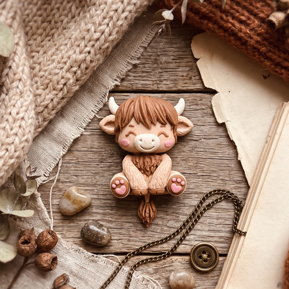 Bébé vache Highland articulé avec chaînette métallique sur un décor en bois