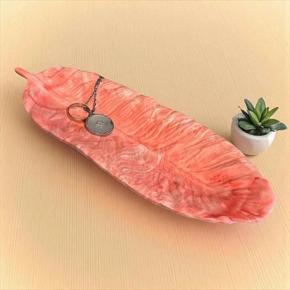Vide-poche en forme de plume rouge clair marbré en Jesmonite, fait main avec texture délicate et finition satinée.
